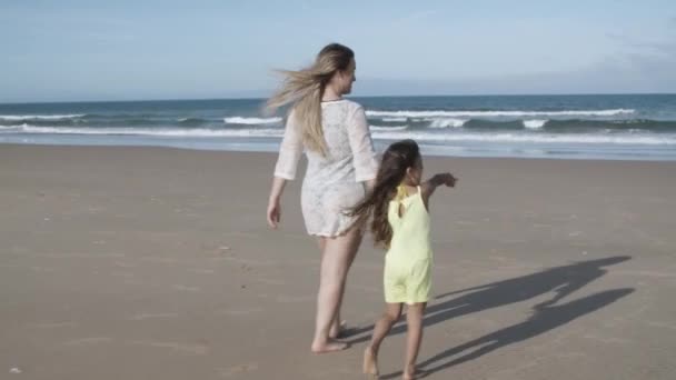 Szczęśliwa mama i mała córeczka spacerujące po plaży do oceanu — Wideo stockowe