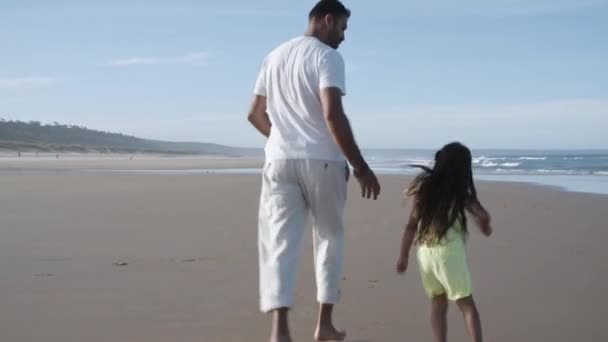 Visszapillantás férfi és kislány fut a strandon a víz — Stock videók