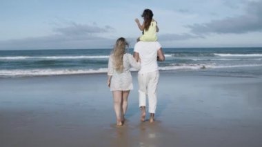Anne babası ve küçük kızı sahilde okyanusa yürüyorlar.