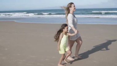 Anne ve küçük kızı sahilde birlikte yürüyorlar.