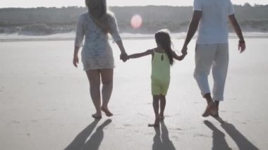 Aile çifti ve yaz kıyafetleri içinde sahilde yürüyen çocuk.