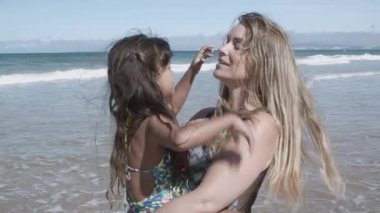 Mutlu anne mayo giyiyor, sahilde duruyor.