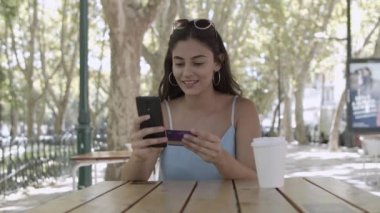 Genç bir kadın akıllı telefondan kredi kartıyla ödeme yapıyor.