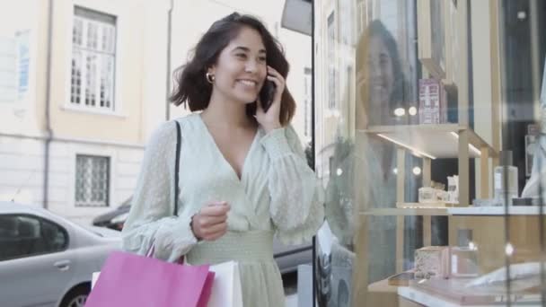 Mujer morena de pie cerca del escaparate y hablando por teléfono — Vídeos de Stock