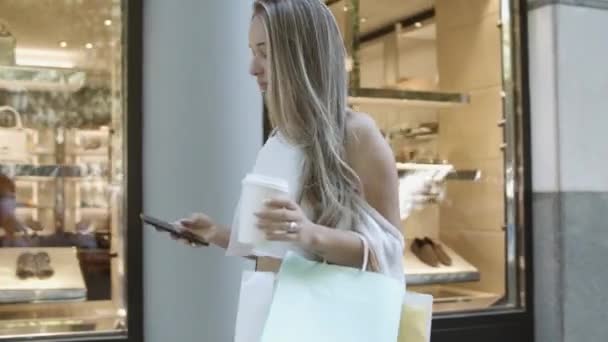 Szőke nő sétál az utcán, és gépel okostelefonon — Stock videók
