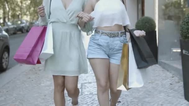 Dos mujeres caminando sobre el pavimento y sosteniendo bolsas de compras — Vídeos de Stock