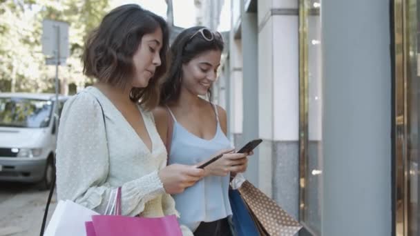 Glückliche junge Frauen, die auf der Straße stehen und ihr Handy benutzen — Stockvideo