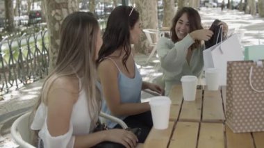 Neşeli kadınlar sokak kafesinde oturuyor ve yeni giysilerini gösteriyorlar.