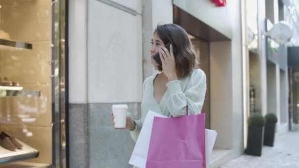 Латиноамериканка разговаривает по мобильному телефону и смотрит витрины магазинов — стоковое видео