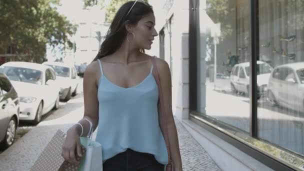 Wanita cantik berambut cokelat berjalan di sepanjang jalan dengan tas belanja — Stok Video