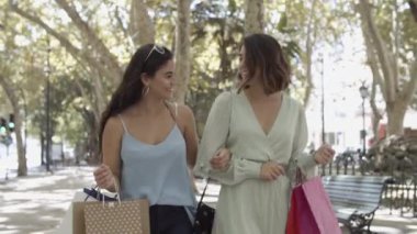 Sokakta alışveriş torbalarıyla yürüyen iki kadının ön görüntüsü.