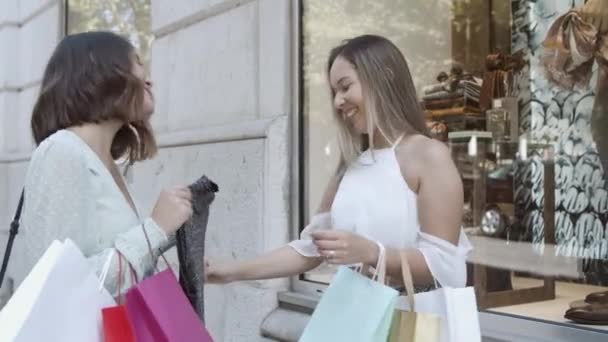 Fröhliche Frauen, die Kleidung aus dem Sack nehmen, anprobieren und lachen — Stockvideo