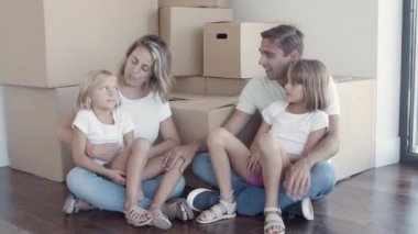 Aile çifti ve iki kız yerde, kutuların yanında oturuyor.