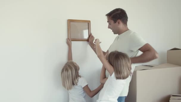 Две девочки и их отец выбирают место на стене для фото — стоковое видео