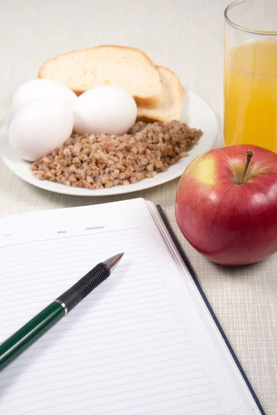 Notebook with buckwheat,bread,eggs,apples and a glass of orange juice.Diet concept