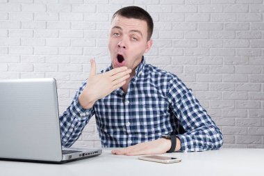 Laptop ile ofiste oturan uykulu yorgun genç adam