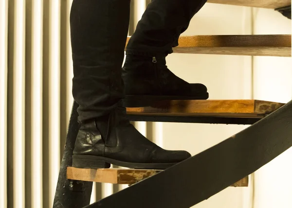 Three steps are seen where one foot of a male is just stepping on a higher step and the other firmly stands on a lower one. Though the image is simple, the contrast of the white and soft colors of the interior and the dark, black color of the boots