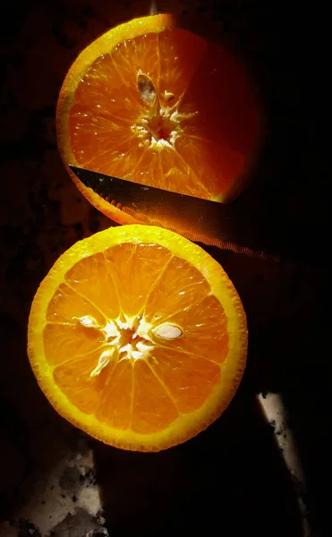 Directly above close up of two sides of an orange cut in two in shadows accompanied with a sharp knife