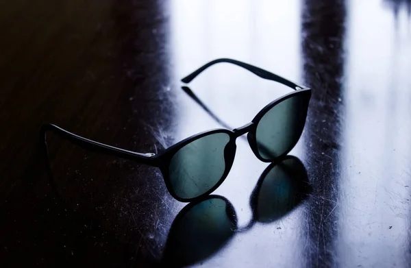 Full frame image of a pair of sunglasses with round black acetate frame standing on scratched, dirty surface. Eyewear and protection concept.