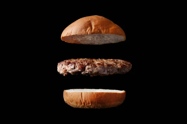 Flying burger with bun and patty isolated on black background — Stock Photo, Image