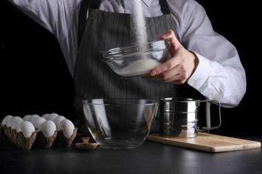 adam siyah arka plan üzerine bir kapta şeker Dökme. pasta yapma kavramı