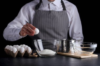 Adam kasede yumurta kırıyor. Koyu arkaplanda turta yapma tarifi