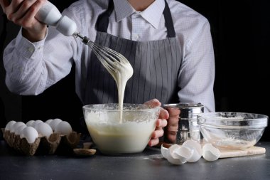 Hamur çırpıcıdan dökülüyor. Adam turta yiyor. Koyu arkaplanda tarif kavramı