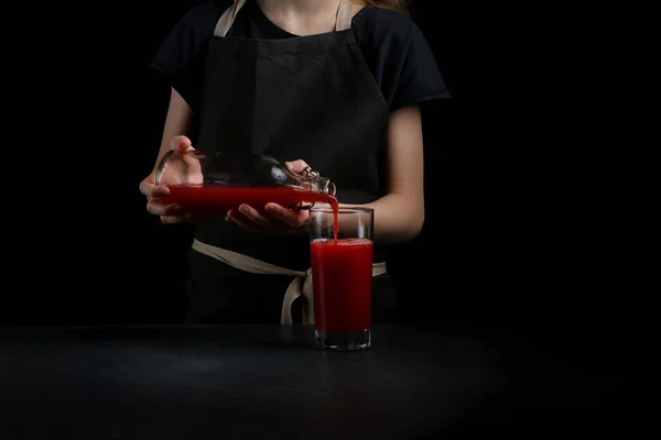 girl pouring juice in glass on dark background. summer drink concept