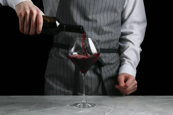 O garçom derrama vinho em vidro no fundo escuro — Fotografia de Stock