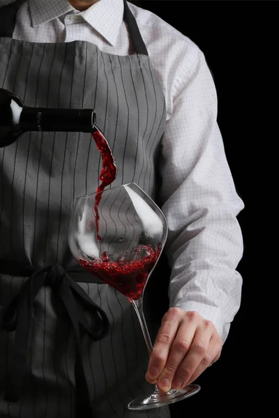 Der Kellner schenkt Wein in Glas auf dunklem Hintergrund ein — Stockfoto