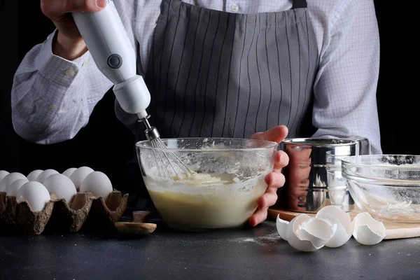 Hamur çırpıcıdan dökülüyor. Adam turta yiyor. Koyu arkaplanda tarif kavramı