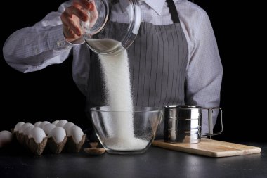 adam siyah arka plan üzerine bir kapta şeker Dökme. pasta yapma kavramı