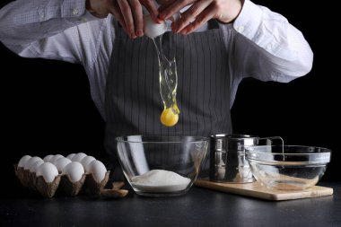 Adam kasede yumurta kırıyor. Koyu arkaplanda turta yapma tarifi