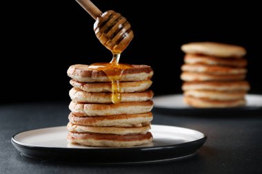 Koyu arka planda bal dökme ile pancake yığını. bal kaşığı