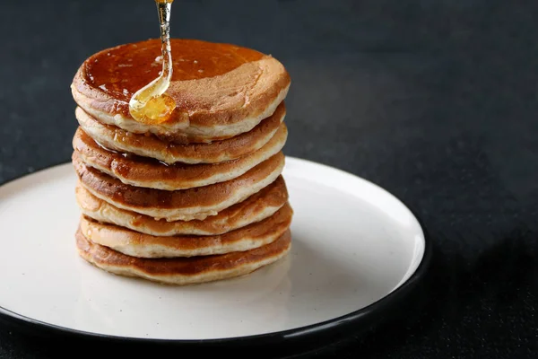 Koyu arka planda bal dökme ile pancake yığını. bal kaşığı