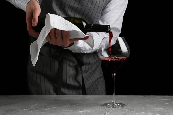 Bartender derrama vinho em vidro no fundo escuro — Fotografia de Stock