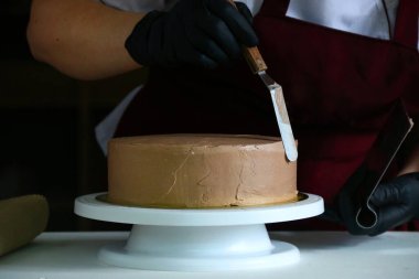 Şekerci masada çikolatalı pasta yiyor. Pastayı sıvı çikolatayla süsleme süreci. Koyu sırtlı çikolatalı pasta yapma süreci.