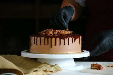 Şekerci masada çikolatalı pasta yiyor. Pastayı sıvı çikolatayla süsleme süreci. Koyu arkaplanda çikolatalı pasta yapma süreci.