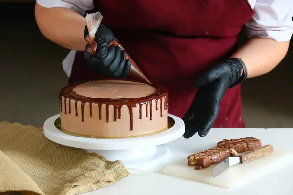 Şekerci masada çikolatalı pasta yiyor. Pastayı sıvı çikolatayla süsleme süreci. Koyu sırtlı çikolatalı pasta yapma süreci.