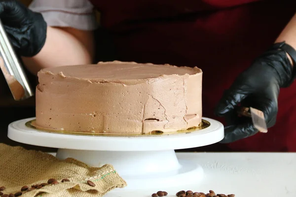 Şekerci masada çikolatalı pasta yiyor. Pastayı sıvı çikolatayla süsleme süreci. Koyu arkaplanda çikolatalı pasta yapma süreci.