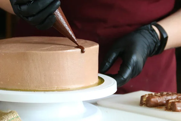 Şekerci masada çikolatalı pasta yiyor. Pastayı sıvı çikolatayla süsleme süreci. Koyu arkaplanda çikolatalı pasta yapma süreci.