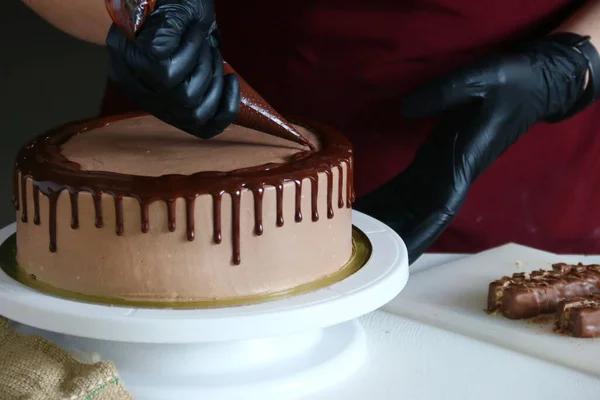Konditor verarbeitet Schokoladenkuchen auf dem Tisch. Der Prozess der Dekoration des Kuchens mit flüssiger Schokolade. Der Prozess der Herstellung des Schokoladenkuchens auf dunklem Hintergrund — Stockfoto
