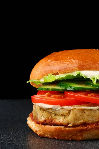 fresh tasty vegan burger on black isolated background. tomato, onion, vegan mayonnaise. Vegan chickpeas burgers with arugula, pickled cucumbers and hummus. Plant based diet concept.