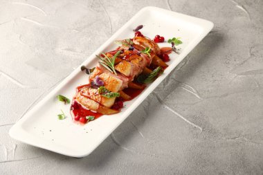 Böğürtlen soslu dilimlenmiş ördek göğsü ve beyaz tabakta mikro yeşil yakın plan ve beton sırt.