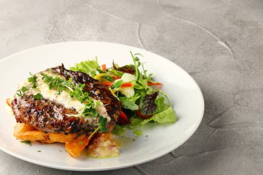 Patatesli ızgara biftek ve salata. Beyaz tabakta yakın plan ve beton sırt.