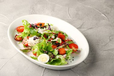 Beton sırtında beyaz tabakta kiraz ve dolma biberli vejetaryen sezarı.