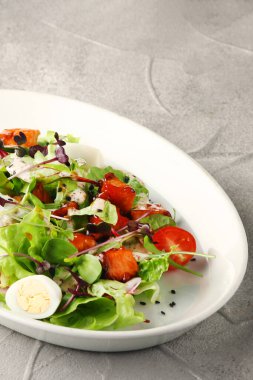 Beton sırtında beyaz tabakta kiraz ve dolma biberli vejetaryen sezarı.