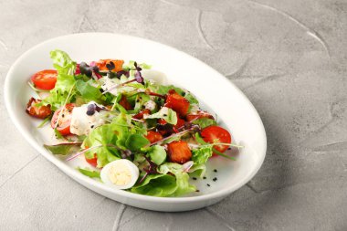 Beton sırtında beyaz tabakta kiraz ve dolma biberli vejetaryen sezarı.