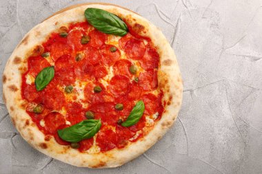 Pepperoni pizza üst görüntüsü ve fesleğen yakın plan beton ya da taş masa ya da sırt. Pepperonili pizza, fesleğen ve kapari.