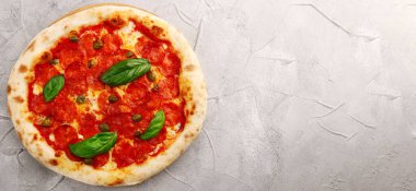 Pepperoni pizza üst görüntüsü ve fesleğen yakın plan beton ya da taş masa ya da sırt. Pepperonili pizza, fesleğen ve kapari.